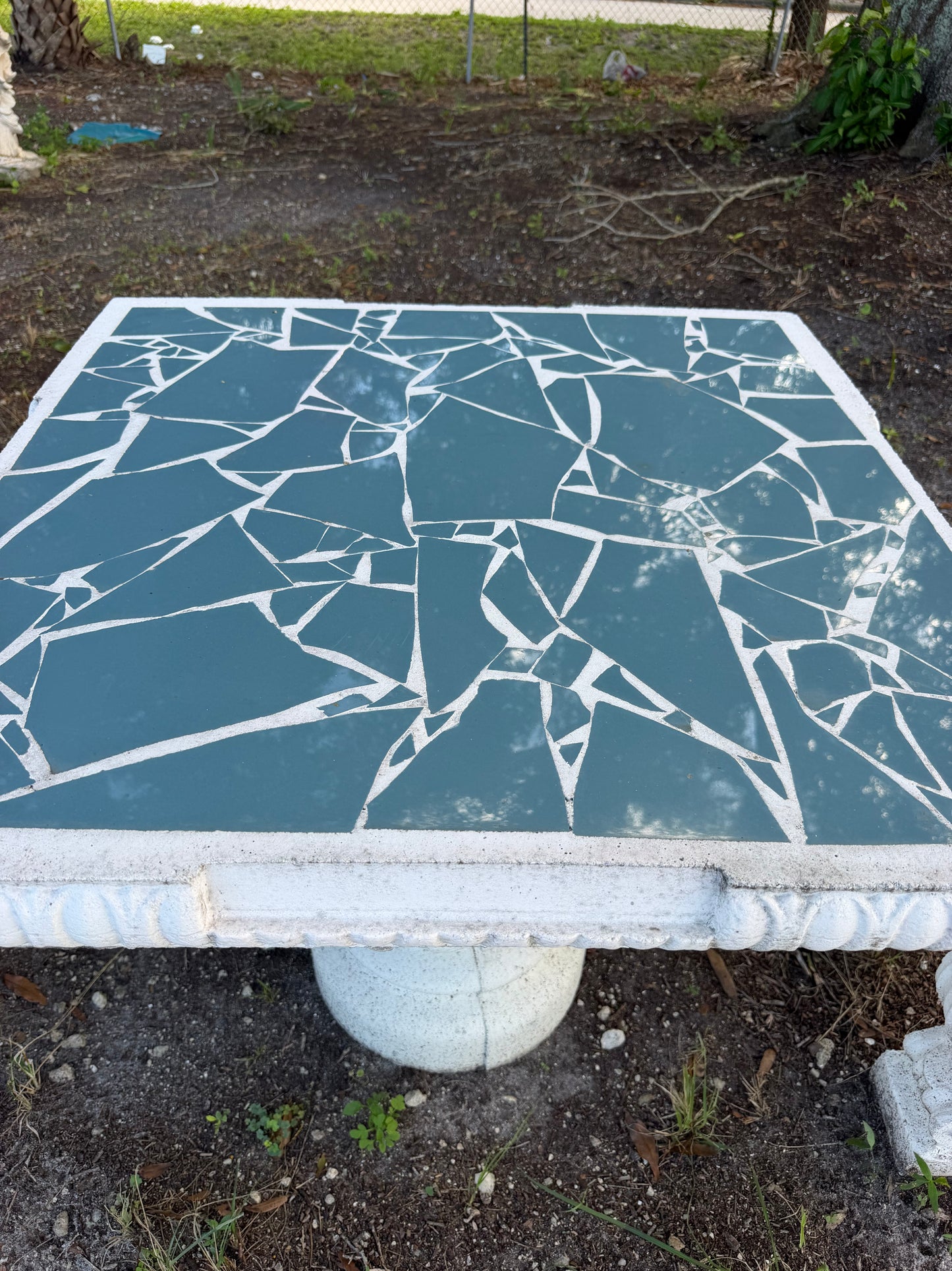 Close-up of the slate blue broken-tile mosaic top and molded edge of a concrete table