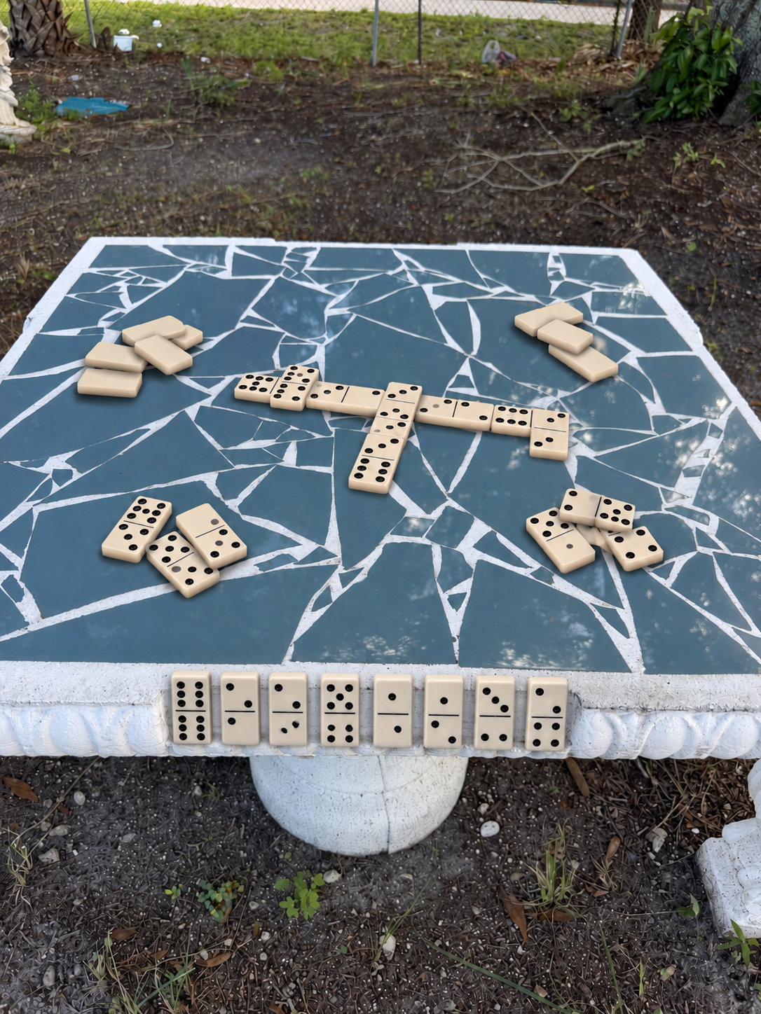 Square concrete domino table with dominoes on its blue mosaic tile top