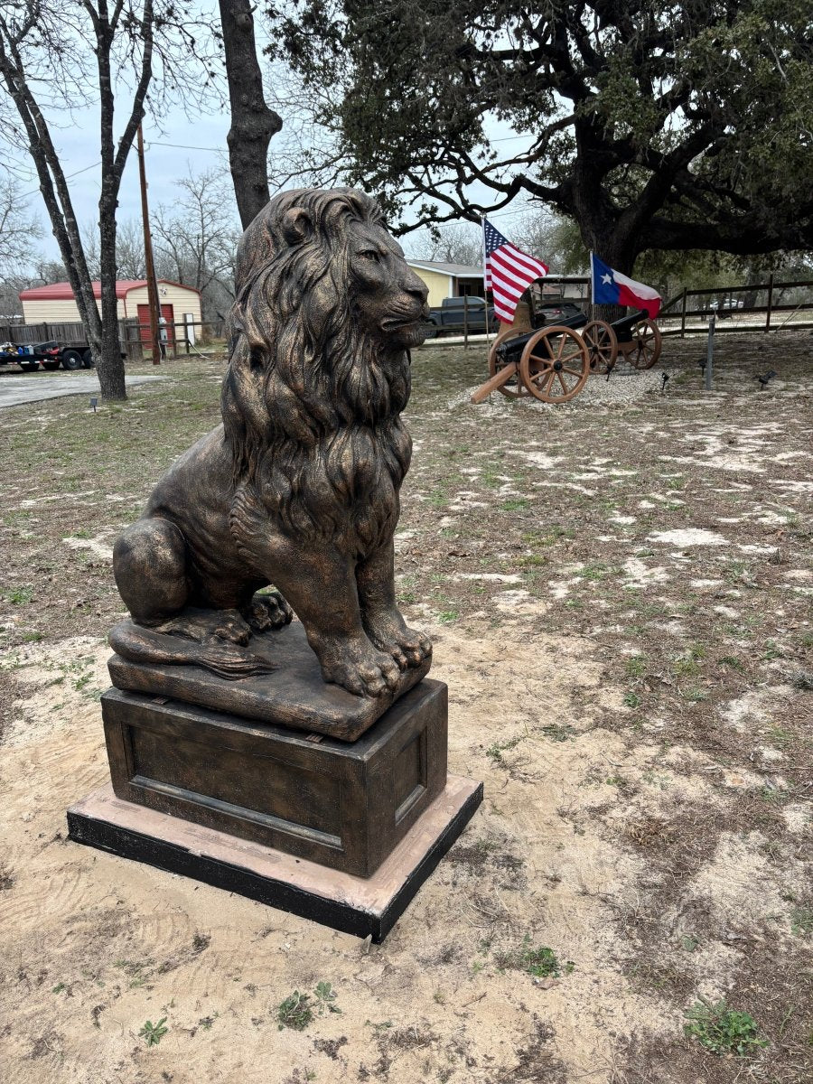 Single bronze concrete lion statue on pedestal in outdoor yard with flags and wagon behind