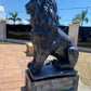 Black concrete lion statue on pedestal standing on brick walkway