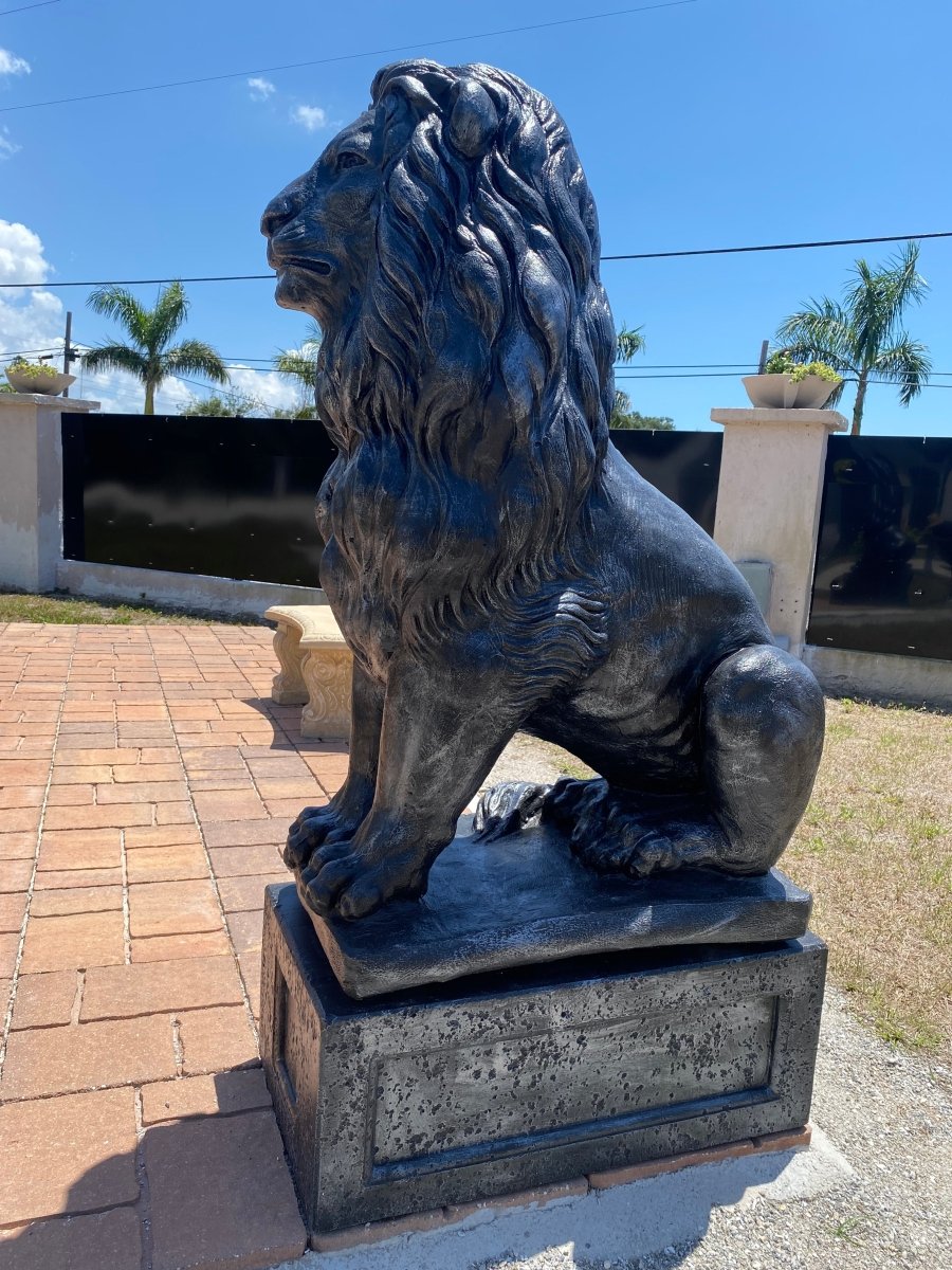 Black concrete lion statue on pedestal standing on brick walkway