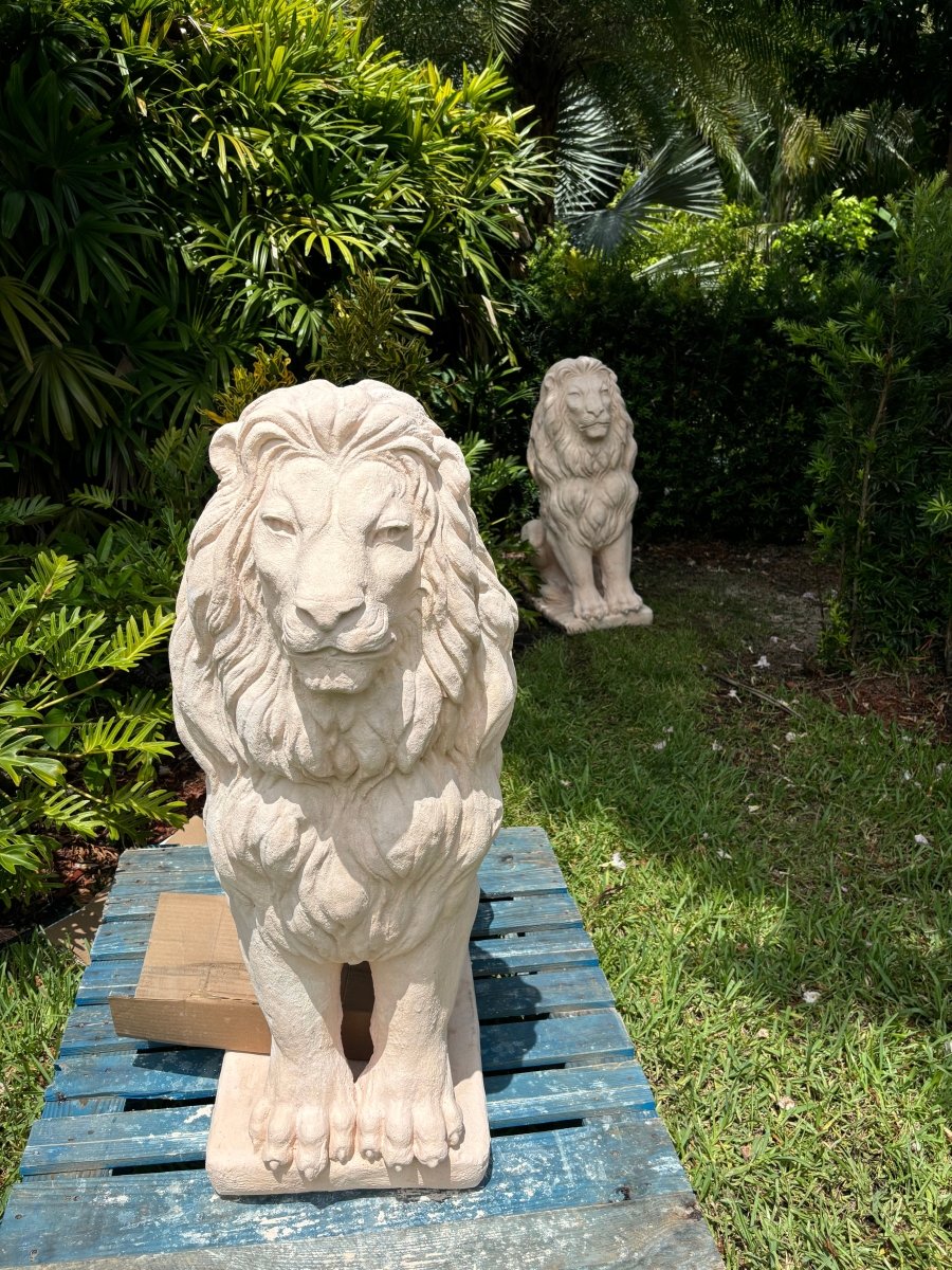Beige concrete lion statue delivered to customers home, in garden with lush greenery and second lion in background