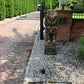 Brown concrete lion statue on pedestal in landscaped yard with gravel path