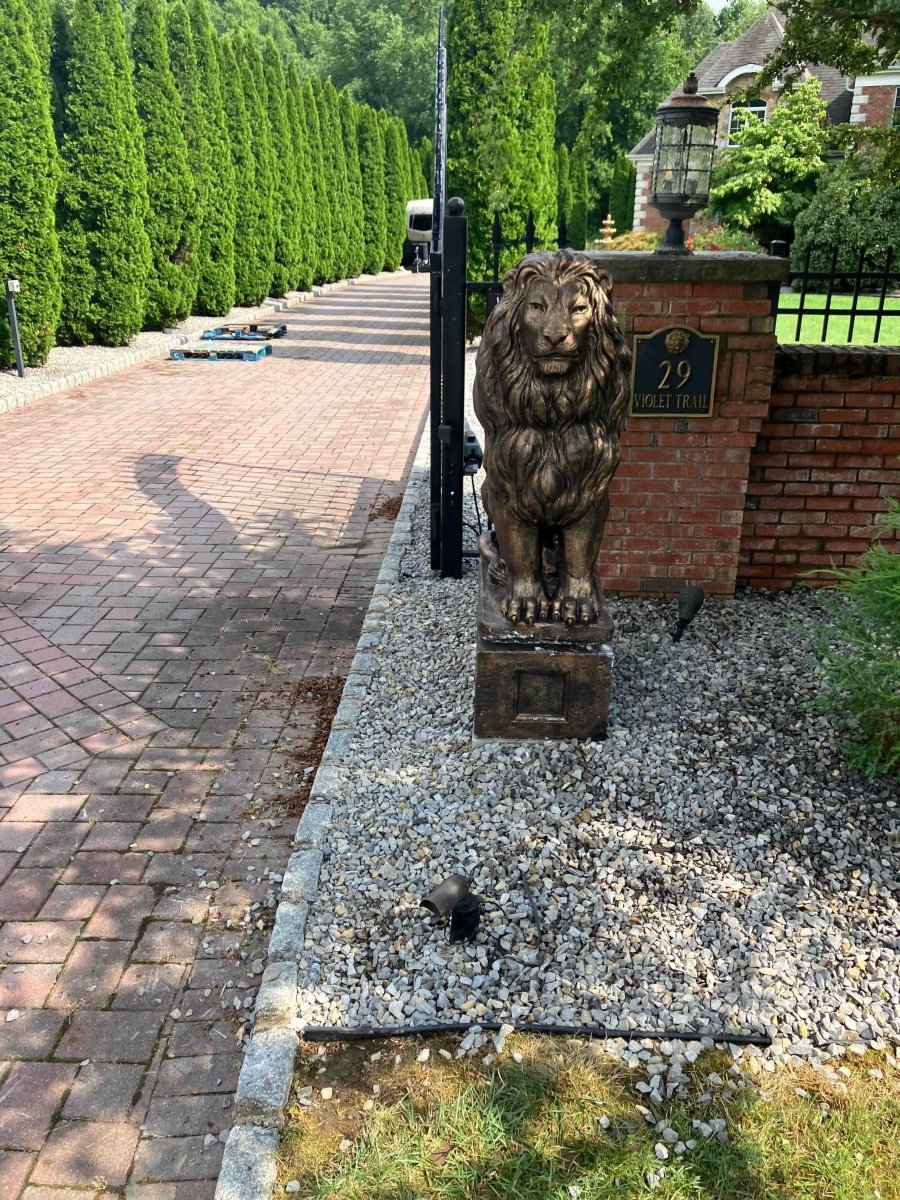 Brown concrete lion statue on pedestal in landscaped yard with gravel path